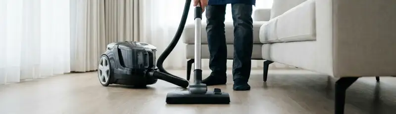Professional house cleaner vacuuming a living room floor with a canister vacuum cleaner, Ogden, UT.
