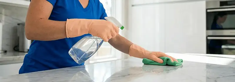 Maid service worker spraying and wiping a kitchen countertop with a microfiber cloth for sanitizing, Ogden, UT.