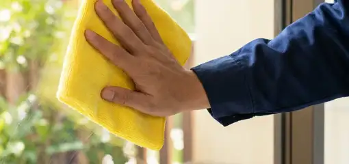 House cleaner wiping a glass window with a yellow microfiber cloth for streak-free cleaning, Ogden, UT.